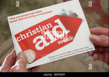 Donna che mantiene la donazione di una moneta per una raccolta di beneficenza busta per Christian Aid settimana Foto Stock