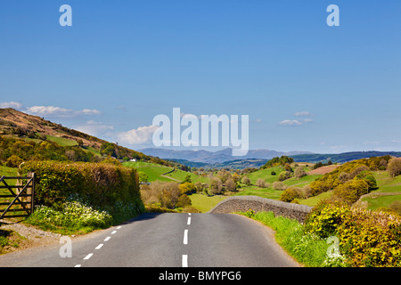 Strada di campagna, Regno Unito. Vista lungo una strada di campagna verso le montagne del Lake District nel Cumbria, Inghilterra, Regno Unito in estate Foto Stock