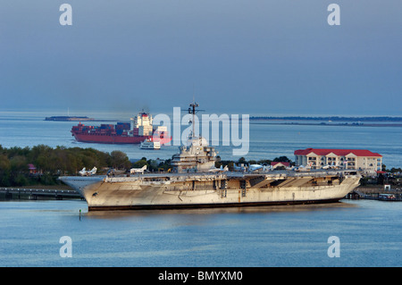 Contenitore nave passando la USS Yorktown al tramonto con il Fort Sumter nella distanza vicino a Charleston, Carolina del Sud Foto Stock