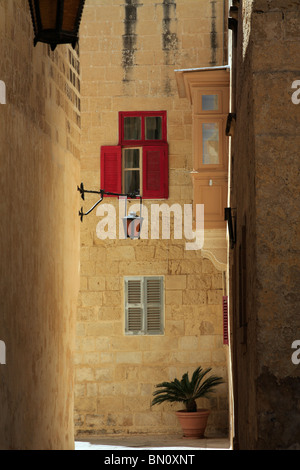 Un vicoletto nelle strade laterali di Mdina, Malta. Alta uo è un rosso finestra ritagliata e marrone chiaro balcone chiuso. Foto Stock