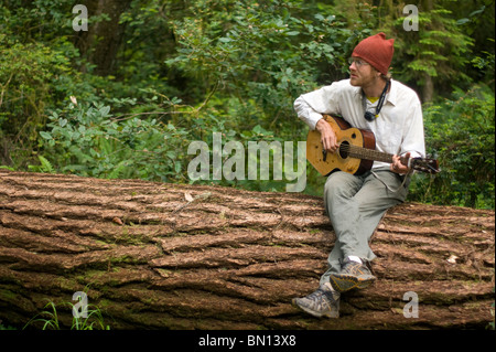 Camping musicisti suonare la chitarra e cantare una melodia in Redwoods Foto Stock