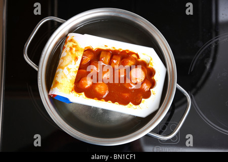 Riscaldamento di pronto a servire i pasti in acqua calda. Minestre o piatti a base di pasta in lattine. La convenienza dei prodotti alimentari. Salsiccia in salsa di pomodoro. Foto Stock