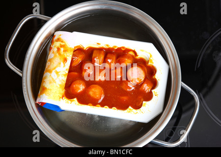 Riscaldamento di pronto a servire i pasti in acqua calda. Minestre o piatti a base di pasta in lattine. La convenienza dei prodotti alimentari. Salsiccia in salsa di pomodoro Foto Stock