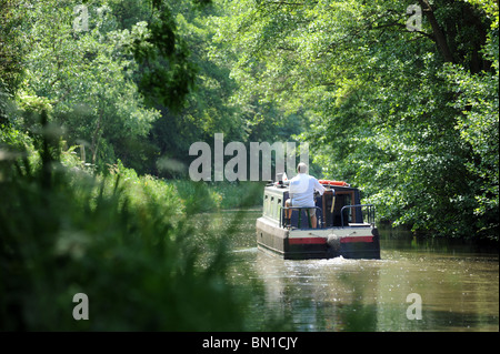 Un uomo percorre una narrowboat lungo un tranquillo tratto di canale in Gran Bretagna, re vacanze pensione tempo libero hobby etc REGNO UNITO Foto Stock