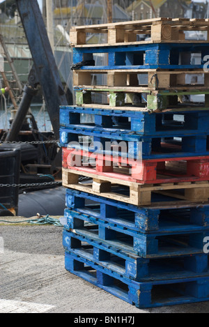 Pesca colorata pallet impilati sul porto di lavoro con la barca in background, Penzance, Cornwall, Regno Unito Foto Stock