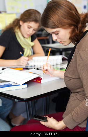 Giovane donna alla messaggistica di testo mentre in classe Foto Stock