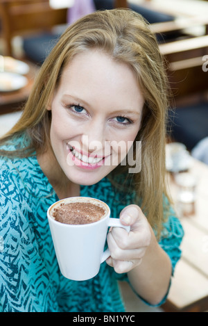 Giovane donna godendo di tazza di cappuccino, ritratto Foto Stock