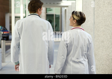 I medici in chat e camminare insieme lungo il corridoio di ospedale, vista posteriore Foto Stock