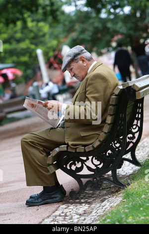 Uomo seduto su una panchina leggendo un giornale Foto Stock