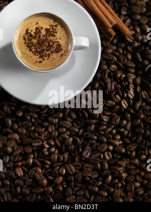 Tazza di caffè latte e bastoncini di cannella in piedi sul caffè in grani sfondo Foto Stock