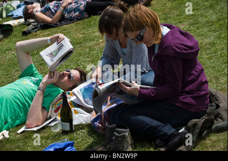 Persone che leggono i giornali seduto o disteso sull'erba sotto il sole a Hay Festival 2010 Hay on Wye Powys Wales UK Foto Stock
