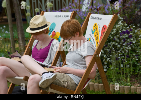 Giovani donne la lettura di libri sat in sedie a sdraio accanto al giardino a Hay Festival 2010 Hay on Wye Powys Wales UK Foto Stock