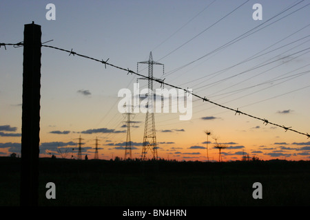 Filo spinato e fili elettrici sono visti nel tramonto su un campo agricolo Foto Stock