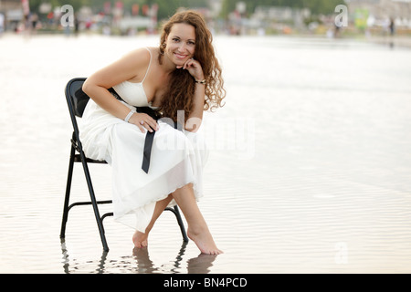 Sorridente bella donna seduta su una sedia in piazza allagata a Bordeaux, Francia Foto Stock
