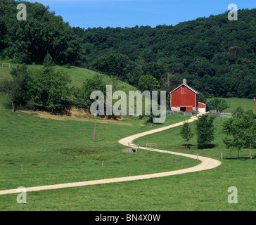 Iowa County, WI curvando strada sterrata che conduce ad un granaio rosso al di sotto di una collina boscosa Foto Stock