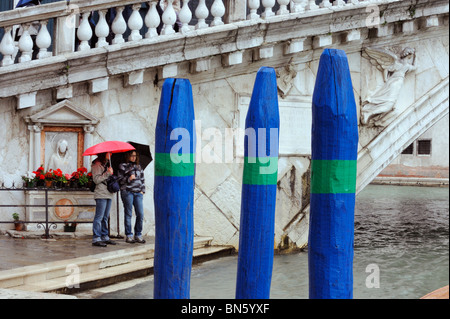 Due turisti in piedi sotto la pioggia dal Ponte di Rialto sul Canal Grande a Venezia Foto Stock