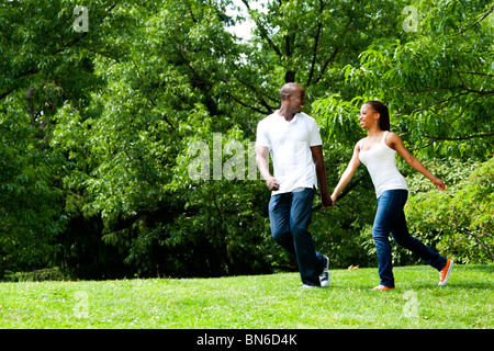 Bella divertente sorridenti americano africano coppia giovane esecuzione di giocare nel parco, indossa camicie bianche e blu jeans. Foto Stock