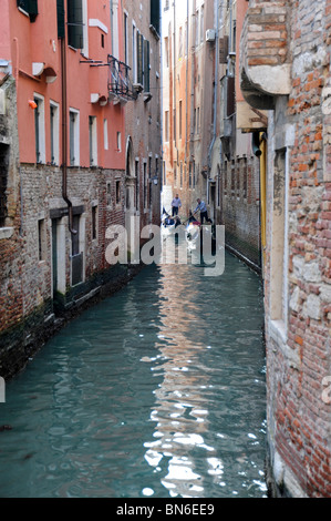 Piccolo stretto canale di Venezia con due gondole in distanza, mostra vecchi edifici veneziani e blu verde acqua. Foto Stock