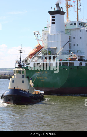 Rimorchiatore manouvering una nave portacontainer a Belfast dock Foto Stock