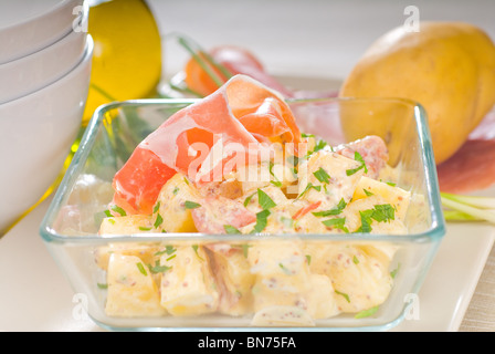 Fresche fatte in casa il prosciutto di Parma e insalata di patate,con materie prime intorno con ciotole e piatti su un tavolo Foto Stock