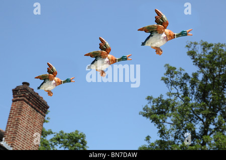 Tre ceramica anatre volanti volare oltre tree tops e camino Foto Stock