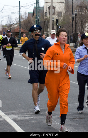 Corridori della maratona vestiti come agenti di polizia a caccia di un sono fuggito di prigione detenuto in una tuta arancione. Foto Stock