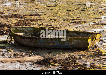 Spiaggiata rotto dinghy a bassa marea amonst alle alghe Foto Stock