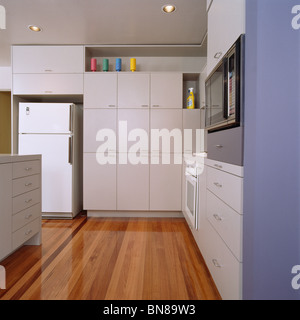 Pavimento in legno bianca e moderna cucina con ampio frigorifero con congelatore e una parete di armadi di archiviazione Foto Stock