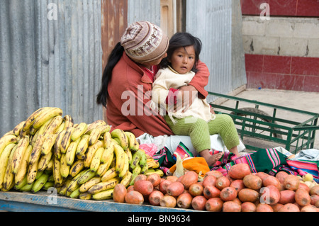 Donna che guarda dopo il suo bambino mentre si lavora su uno stallo del mercato per la vendita di frutta Foto Stock