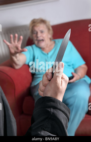 Coltello tirato come terrorizzato donna anziana guarda verso il pirata informatico Foto Stock