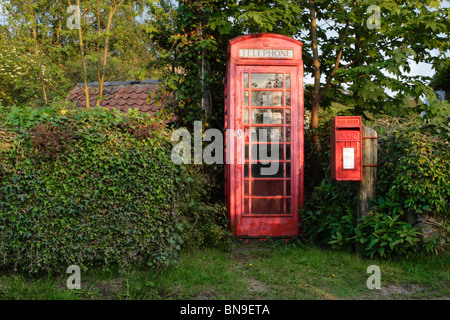 Un trascurato cercando inglese tradizionale telefono rosso scatola e ben mantenuto red post box in una posizione rurale Foto Stock