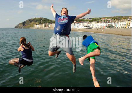 Tre adolescenti il salto in mare al largo del molo sulla spiaggia a Aberystwyth Wales UK in un caldo giorno d'estate, Foto Stock