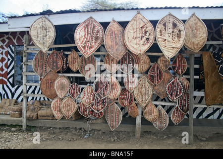 Masai maschere di legno e artigianato tradizionale gli elementi che sono venduti a un negozio di souvenir vicino alla Riserva Nazionale di Masai Mara Kenya, Africa orientale Foto Stock