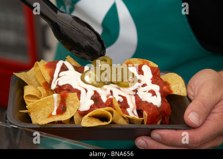 L'uomo servono freschi nachos con salsa e peperoncini jalapeno su un fast food in stallo un mercato Foto Stock