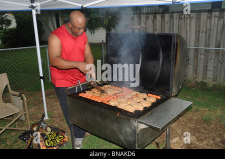 L'uomo grigliare hamburger e hot dogs sulla griglia esterna Foto Stock