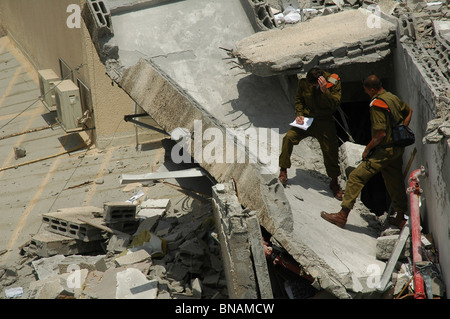 Gli ufficiali israeliani dalla ricerca e salvataggio stand dei vigili del fuoco in mezzo alle macerie di un distrutto edificio residenziale dopo aver subito un colpo diretto da un Hezbollah grad razzo sparato dal Libano nella città di Zafed il nord di Israele Foto Stock