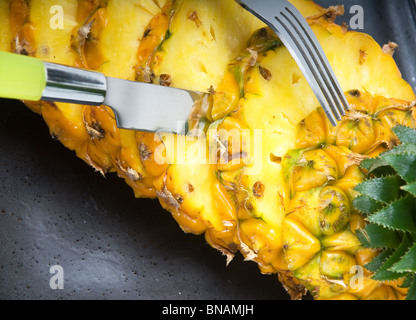 Mature vivaci a fette di ananas su una piastra nera con coltello e forchetta Foto Stock