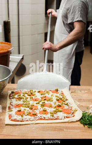 Lo chef maschio rendendo la pizza in cucina commerciale Foto Stock