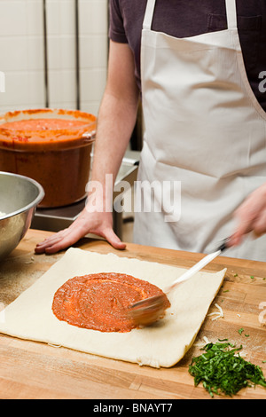 Lo chef maschio rendendo la pizza in cucina commerciale Foto Stock