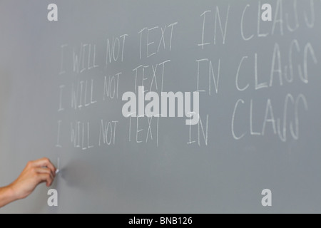 Maschio di alta scuola studente linee di scrittura sulla lavagna Foto Stock