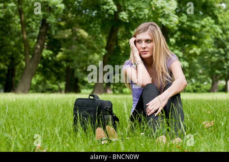 Giovani preoccupati business donna ubicazione in erba - borsa per notebook e scarpe che giace accanto Foto Stock