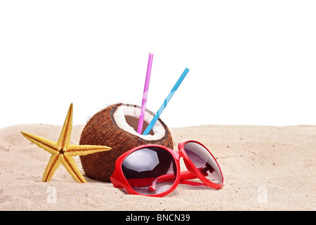 Una noce di cocco, stelle marine e un paio di occhiali da sole su di una spiaggia Foto Stock