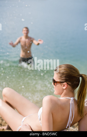 Coppia giovane godere giorno di estate sulla spiaggia da mare, uomo in background gli spruzzi di acqua Foto Stock