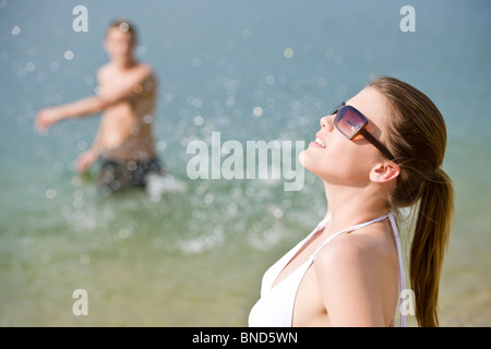 Coppia giovane godere giorno di estate sulla spiaggia da mare, uomo in background gli spruzzi di acqua Foto Stock