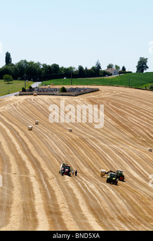 Foto di stock di trattori la raccolta di frumento e rendendo le balle di paglia in Francia. Foto Stock