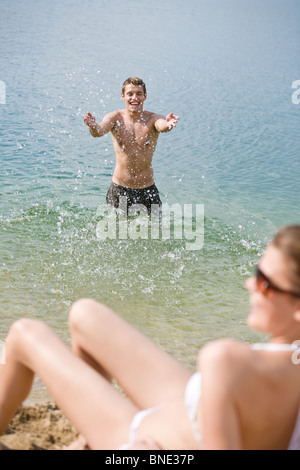 Attività sportive giovane godere di sole estivo sulla spiaggia, l'uomo in background gli spruzzi di acqua Foto Stock
