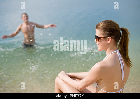 Coppia giovane godere di sole estivo sulla spiaggia, l'uomo in background gli spruzzi di acqua Foto Stock