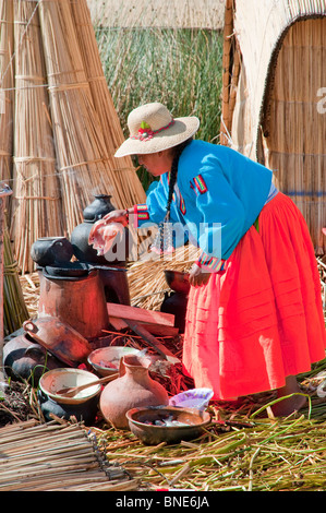 Una donna in abito tradizionale cucinare un pasto sull'isola galleggiante di Uros nel Lago Titicaca, Perù, Sud America. Foto Stock