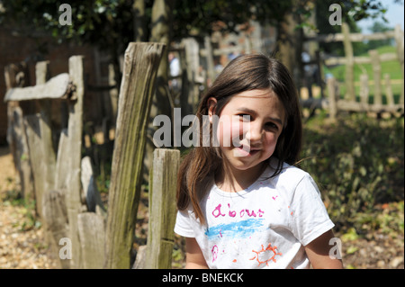 Dark capelli lunghi poco ragazza seduta in un parco in estate indossa un white t shirt con il sole su di esso. Lei è sorridente. Foto Stock