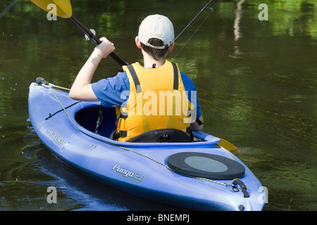 Un giovane ragazzo caucasico in un kayak con giubbotto salvagente e attrezzi da pesca. Foto Stock